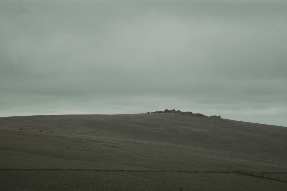 A washed out view across some fields towards a Tor. There is nothing remarkable in the image.