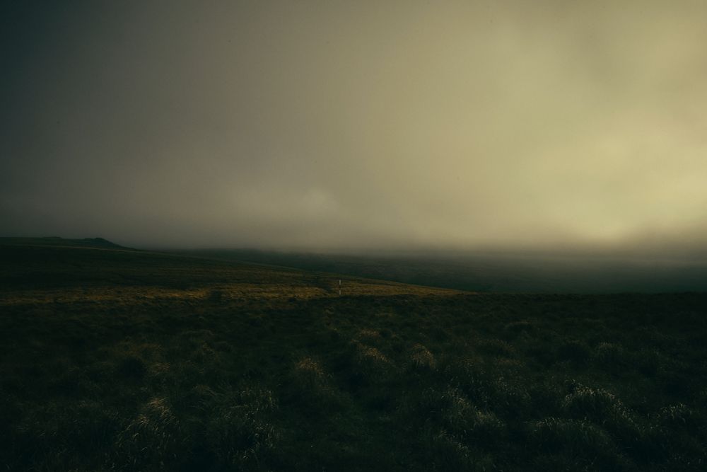 Looking over a high plateau on Dartmoor. Low cloud obscures the horizon. A solitary red and white pole stands in the middle.
