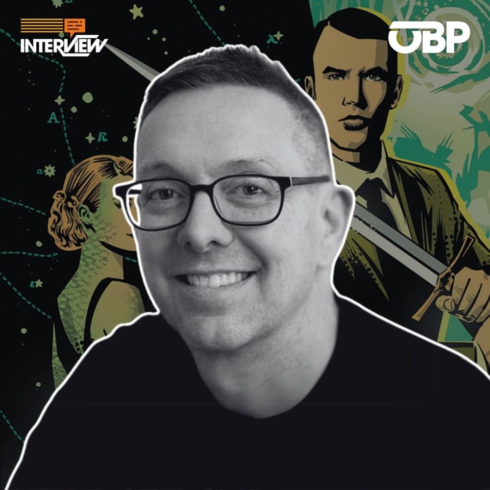 Black and white photo of a comic creator with a sword-wielding man in a suit & tie in the background.