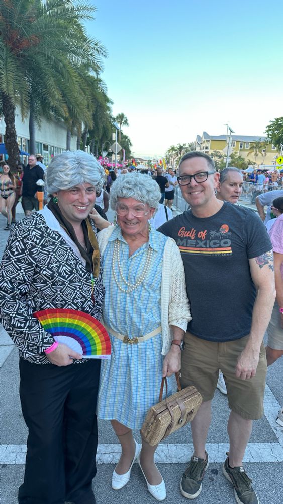 A man in a Gulf of Mexico tee shirt with two men dressed as Golden Girls at a gay pride parade.