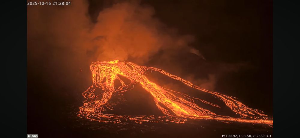 Webcam photo of a glowing lava flow and gas plume at night. 
