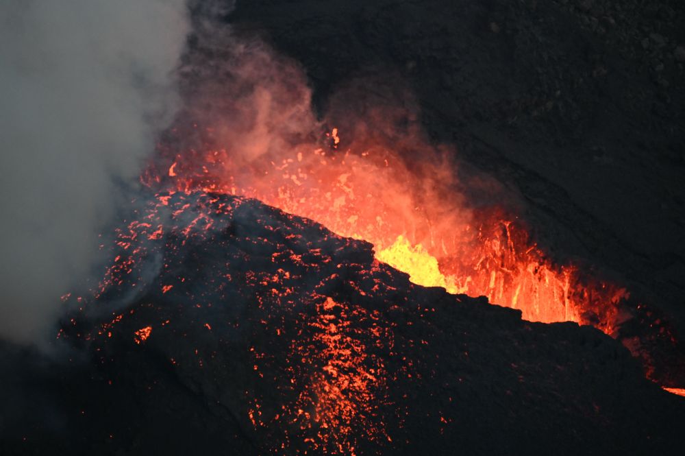 A roiling volcanic vent with orange lava glow and some spatter glowing on the side. 