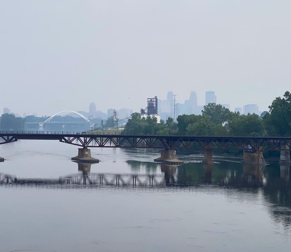 Scene from the Canden Bridge in North Minneapolis, looking out at the Mississippi River. The Minneapolis skyline is grey and draped in a haze.