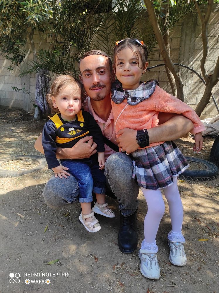 Ahmed crouching with his arms around Wateen and Noor. They're all smiling.