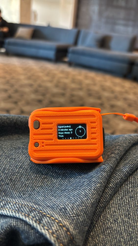 A bright orange Meshtastic radio in an AlleyCat 3d printed case for a Heltec v3 LoRa radio, bough at Shmoocon.