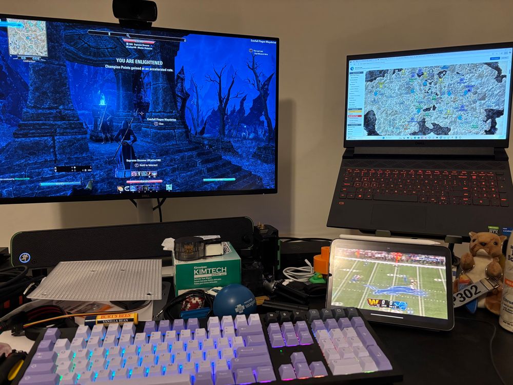 Photo of my desk with a larger monitor showing Elder Scrolls Online's Coldharbour realm, a laptop display with a map of Coldharbour, and an iPad showing FOX Sports' coverage of the Commanders at Lions football game.