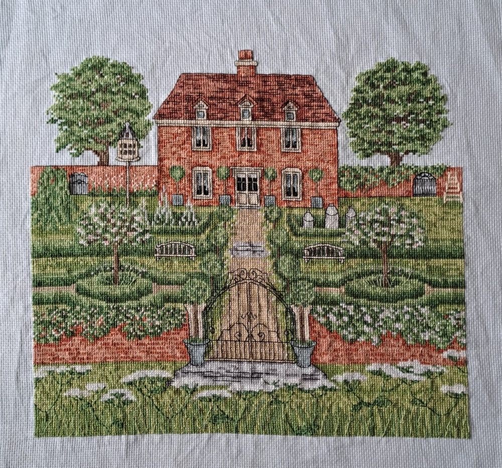 A completed cross stitch of a brick manor house and gardens