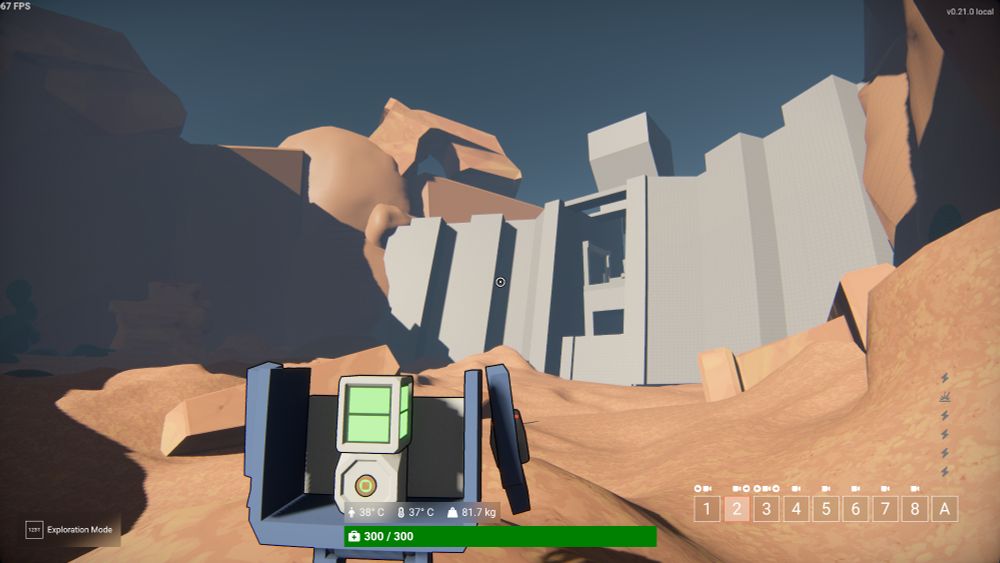 A robot character stands on a dry, rocky, beige riverbed looking up at a large grey dam.