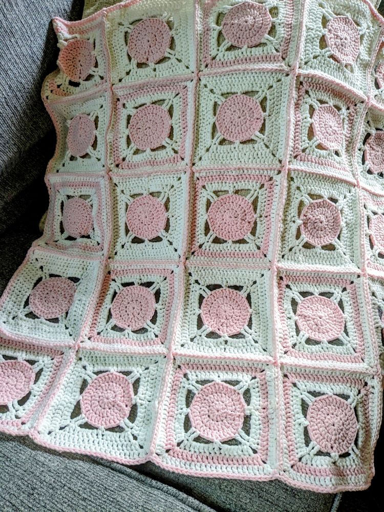 A pink and white granny square baby blanket 