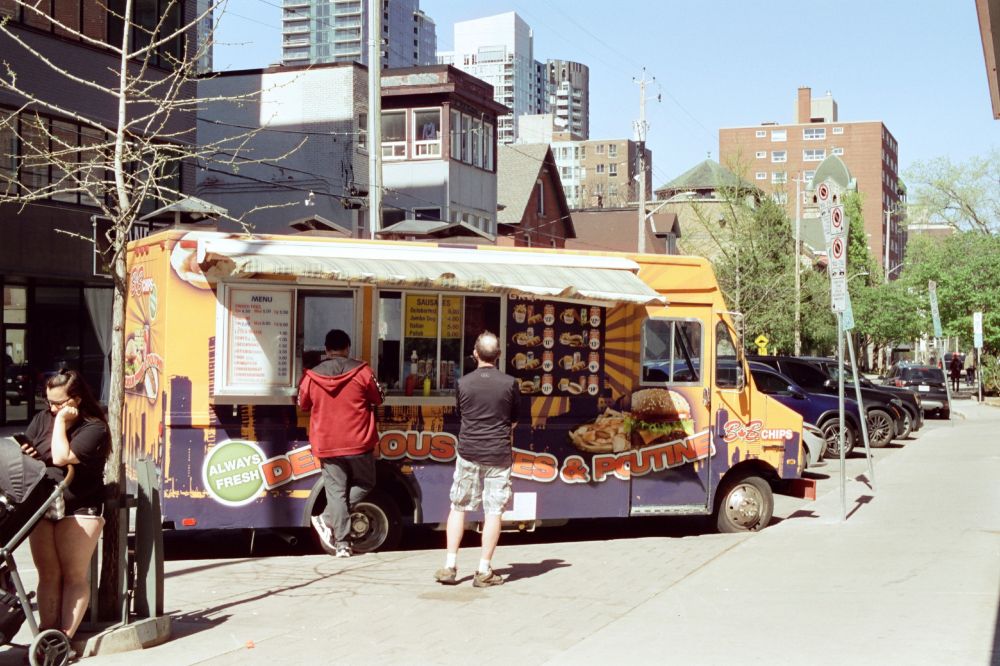 Patrons line up outside of a chip truck. A woman with a stroller scrolls her phone as she waits for her order.