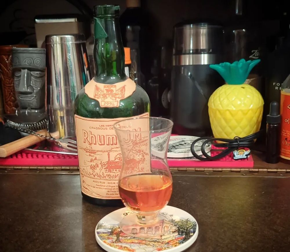 A glass of Rhum JM 1994 Rhum. Agricole Vieux sits in front of a dusty bottle. 