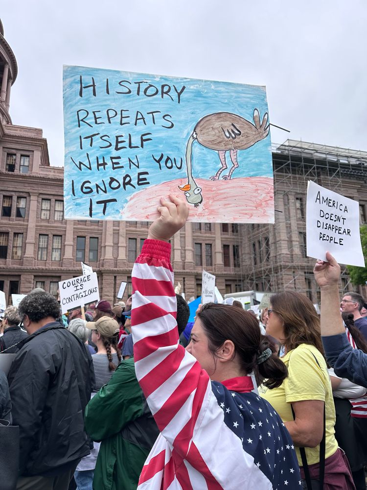 Protest scene with sign that says History repeats itself when you ignore it. 