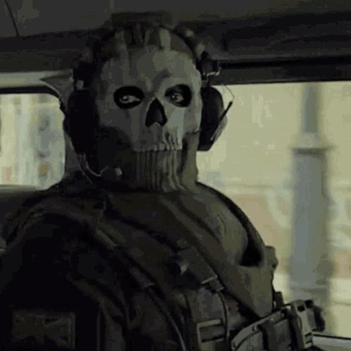 a soldier with a skull mask and headphones is sitting in a car .