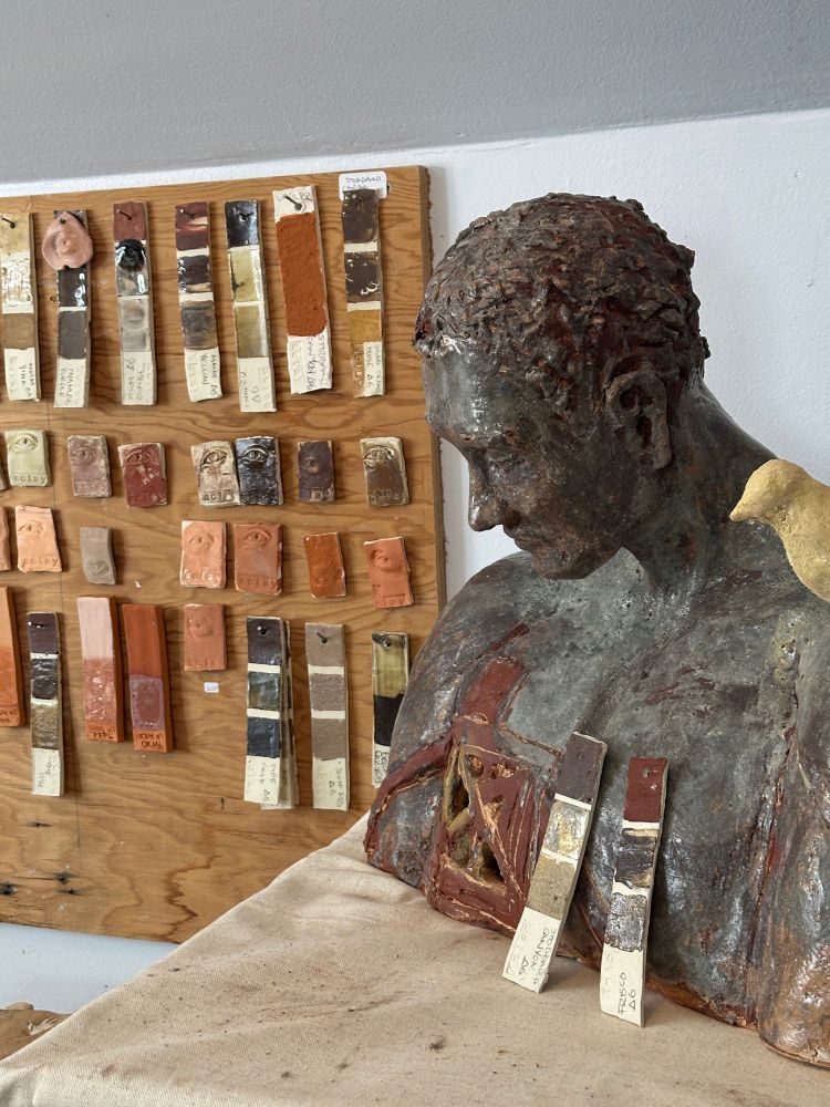 Ceramic bust with blueish and red cast in foreground, test tiles in background.
