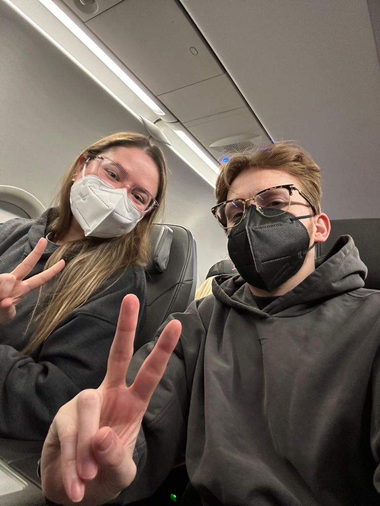 GlitterXplosion and Dan Gaskin holding up peace signs sitting in their seats on a plane
