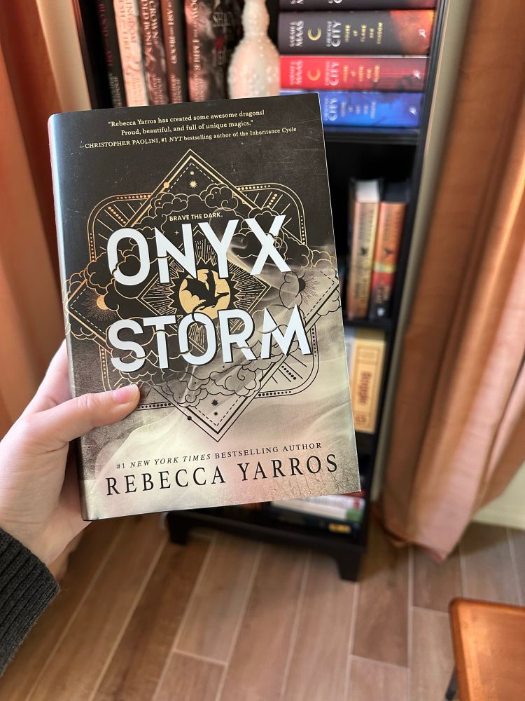 A picture of the new book, Onyx Storm, by Rebecca Yarros in front of a bookshelf