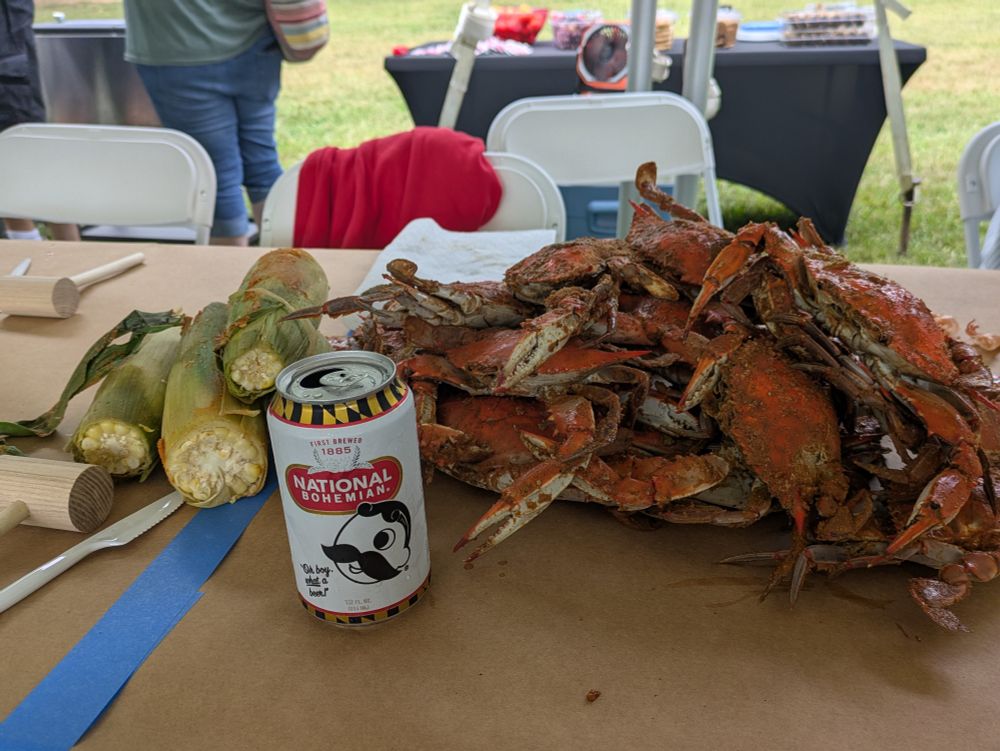 A huge pile of crabs and some corn and Natty Boh on a table covered with paper