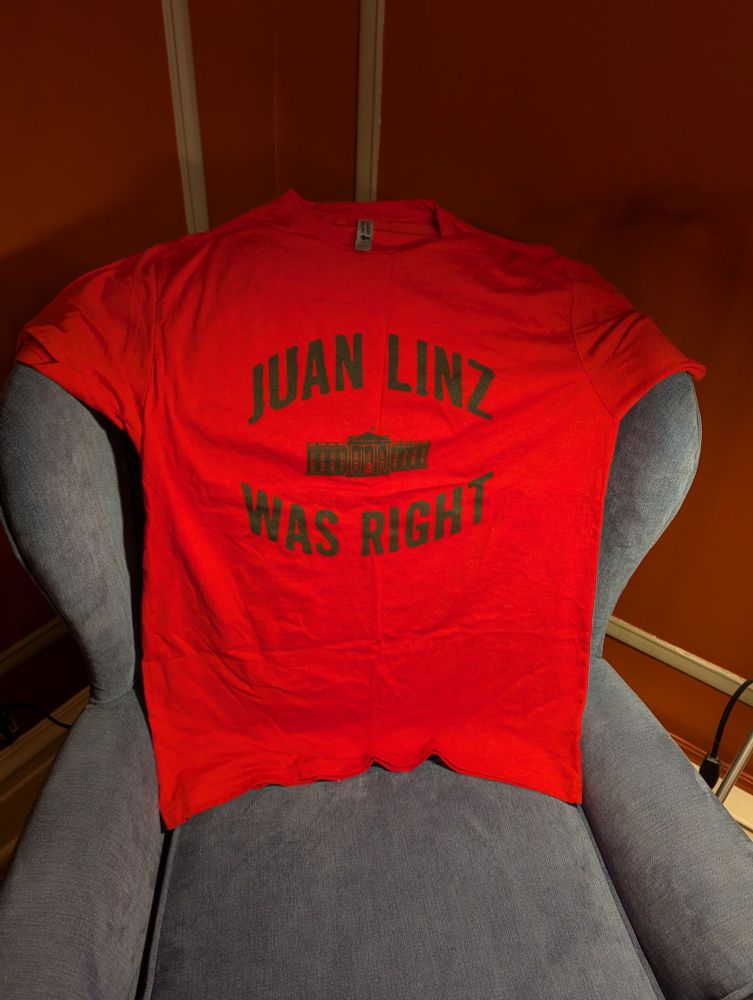 A picture of a red t shirt on a blue arm chair. On the shirt is written "Juan Linz was right" with a picture of the White House among the letters.