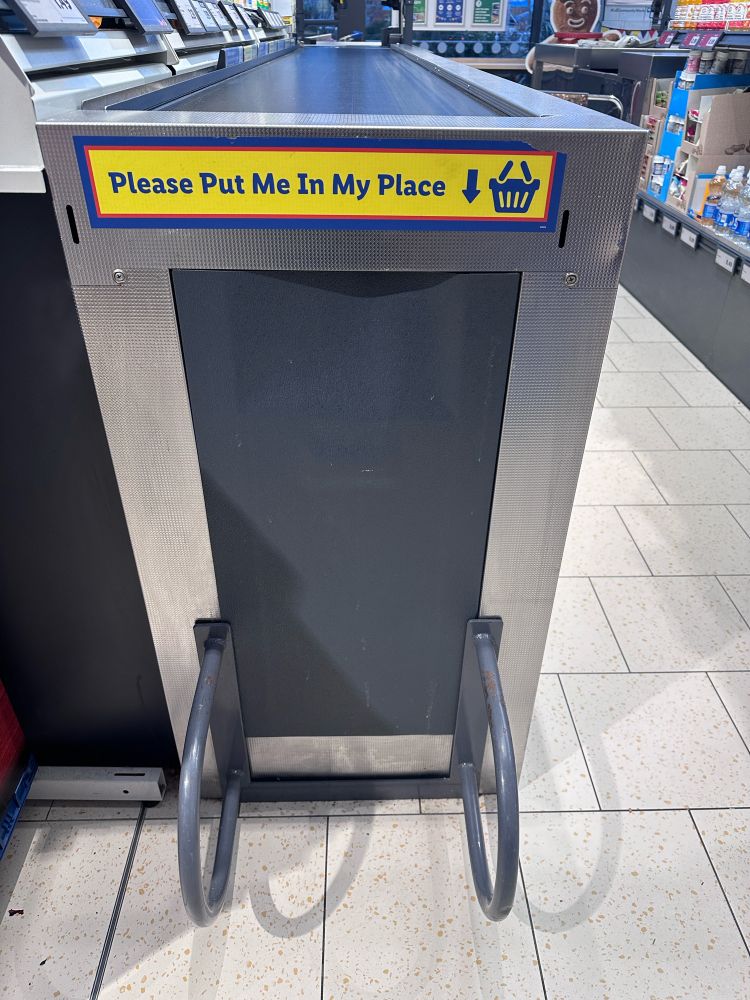 Shopping basket holder in Lidl witb the words “please put me in my place” above it. 