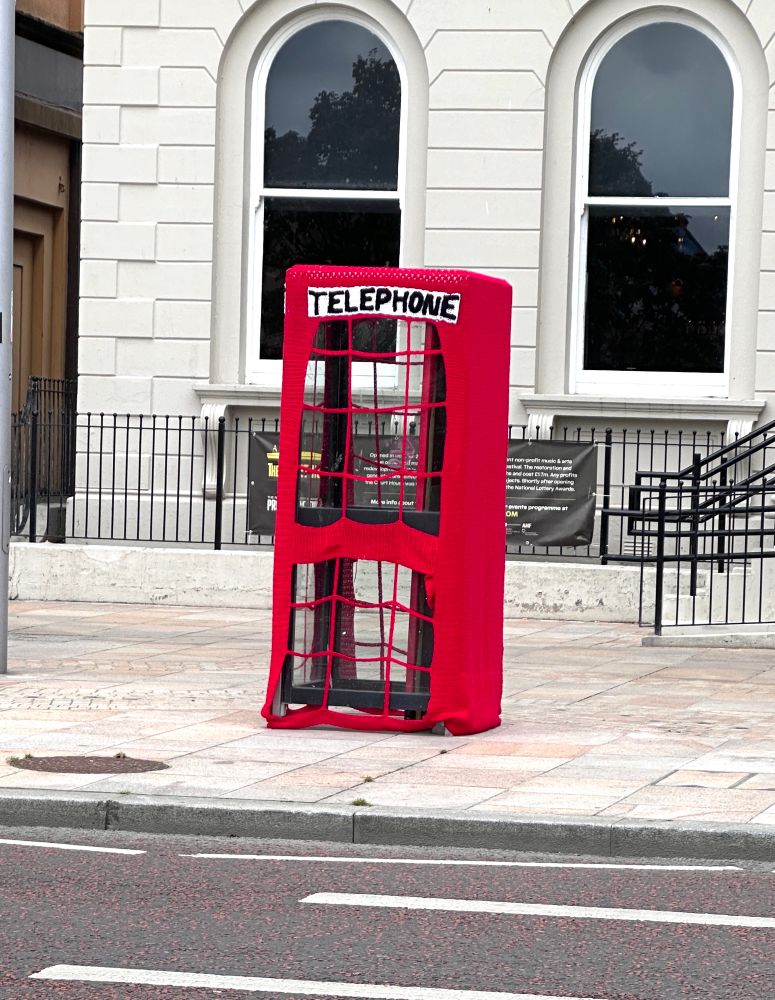 What the tweet says! A red knitted cover for a phone box to make it look like an old phone box, complete with window panes around the sides. 