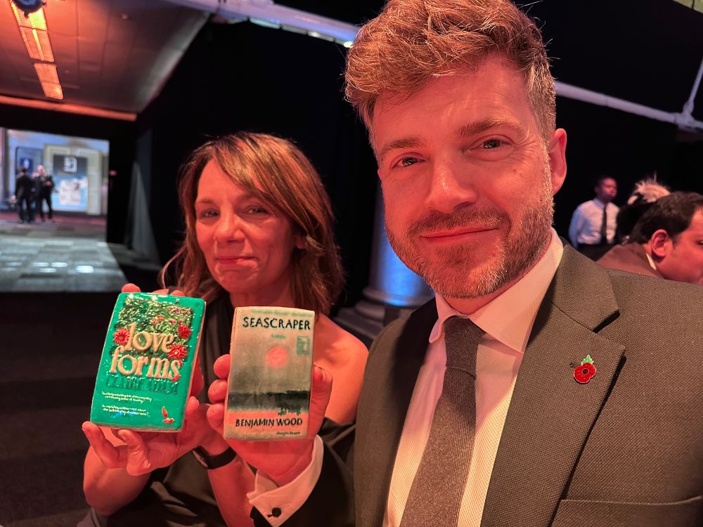 The authors in question smiling and holding up miniature glazed versions of their covers