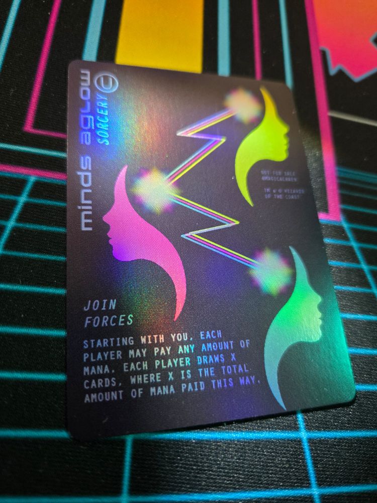 Photo of a foil mtg proxy card of Minds Aglow, the art depicts 3 faces in profile, connected by colored lines and bursts of light