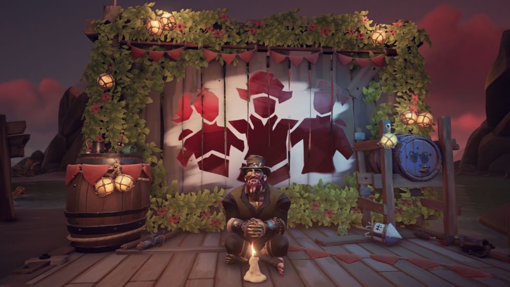 A pirate from Sea of Thieves sitting legs crossed in front of a photowall showing the community weekend emblem. The pirate has a candle on the ground in front of them.