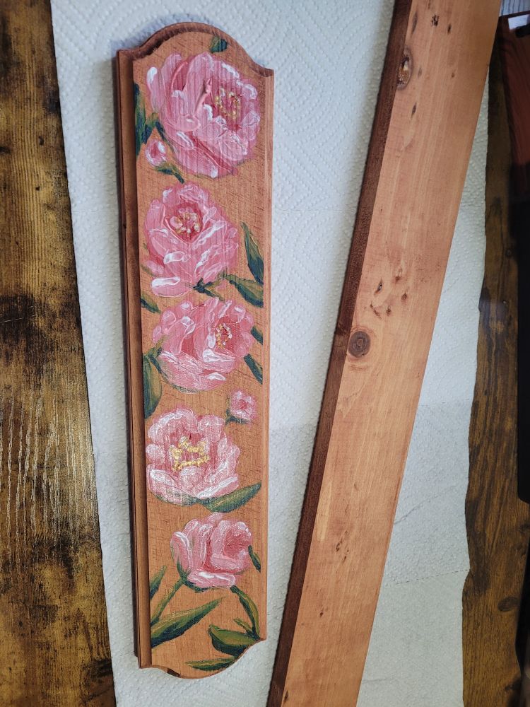A image of two pieces of wood on a paper towel spread. Both have been newly stained. One is painted in pink flowers with green leaves