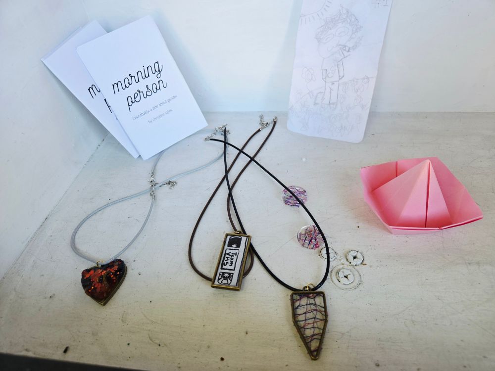 A box with a pencil drawing, origami, some necklaces, buttons, and zines 