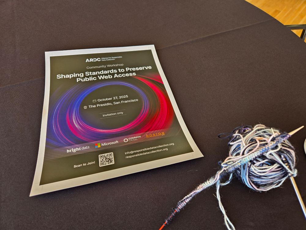 A poster with a red and purple swirl on it and the text "Shaping standards to preserve public web access", with a ball of yarn and knitting needles with a new project next to it 