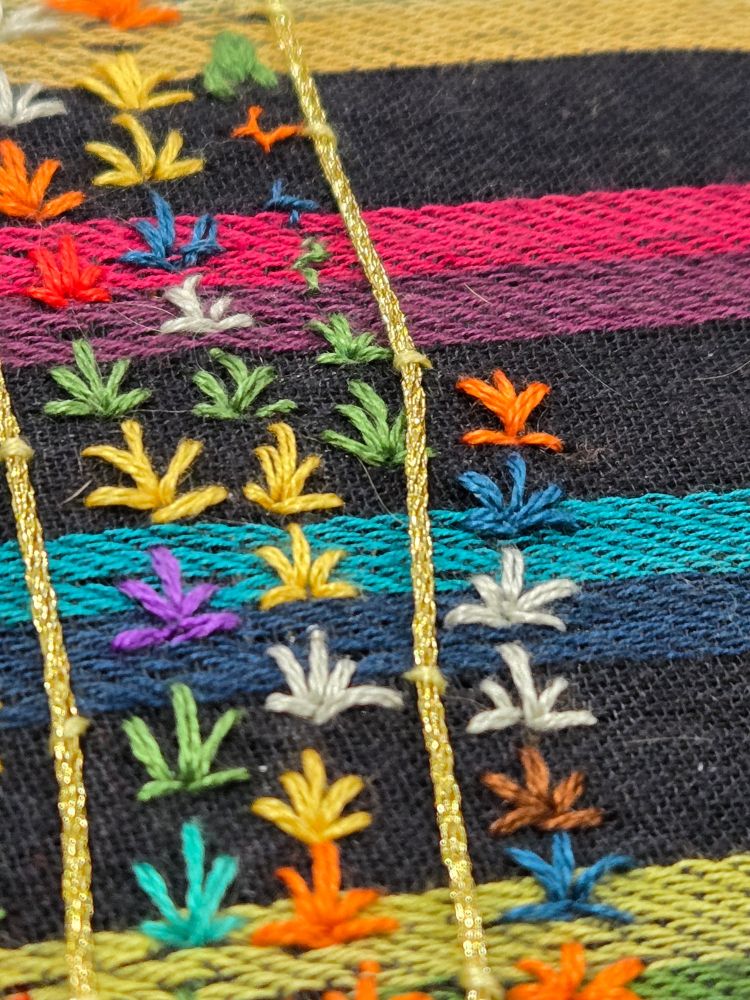 Rows of colorful stitches in the shape of plants mostly on rainbow striped fabric 