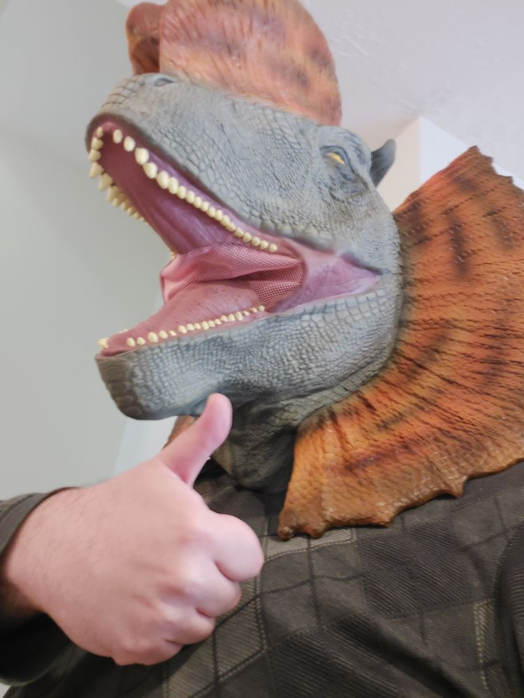 Photo of a guy wearing a dinosaur mask giving a thumbs up.