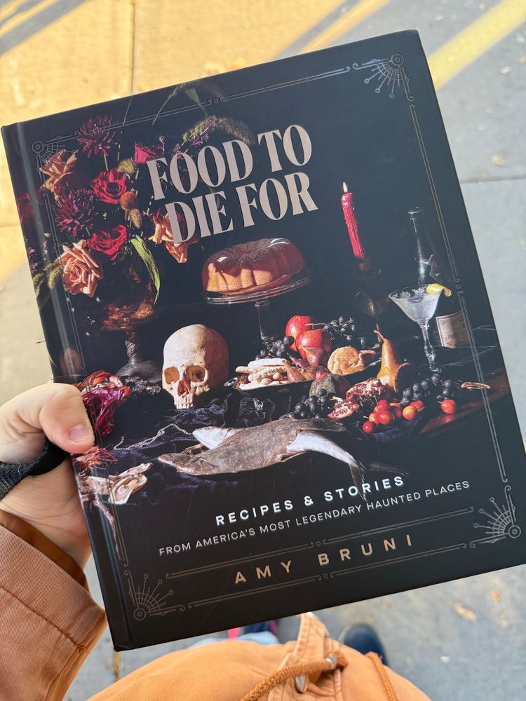 Me holding a hardcover copy of the haunted cookbook “Food to Die For” by Amy Bruni. 