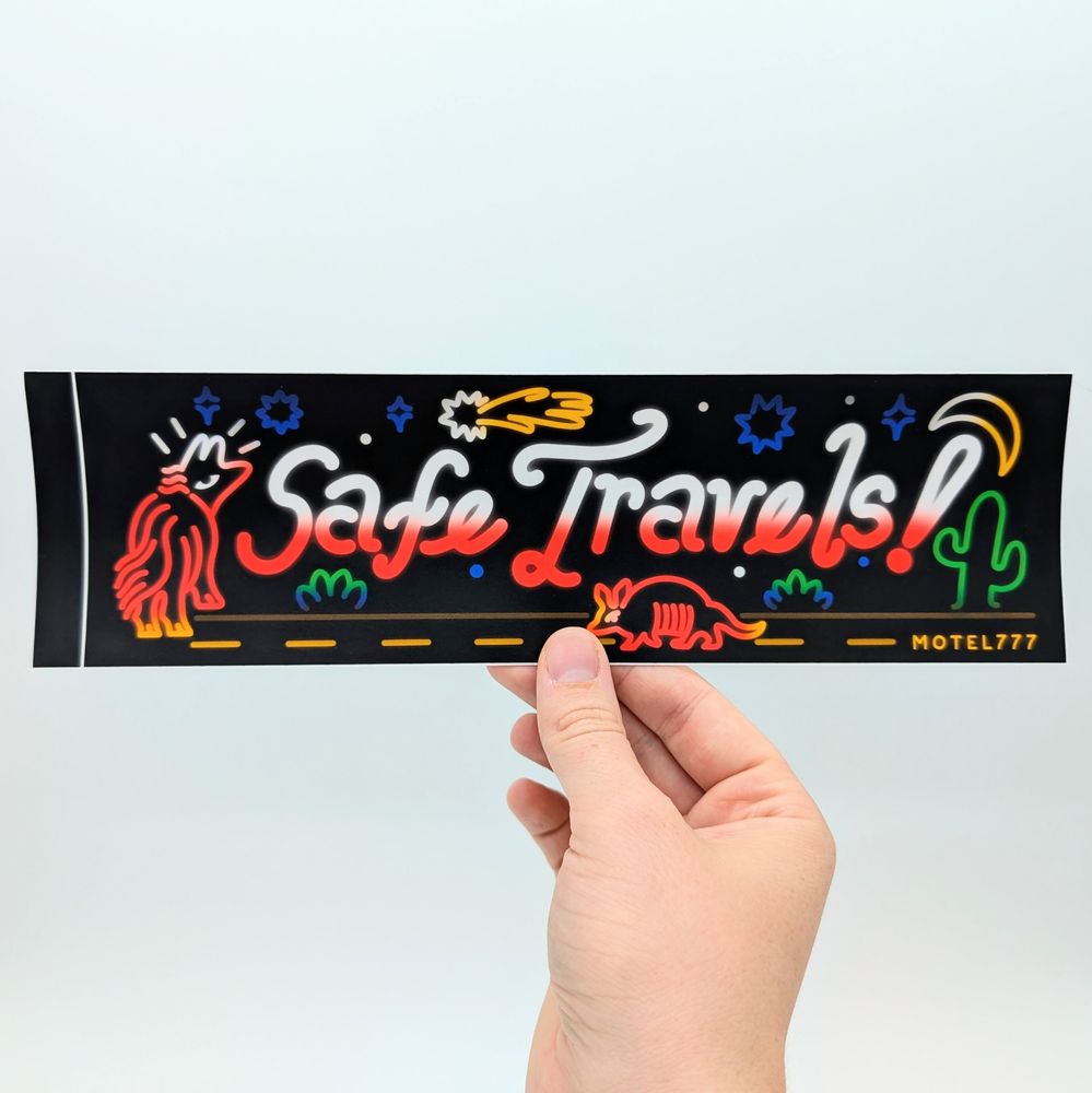 A hand holding up the Safe Travels bumper sticker.