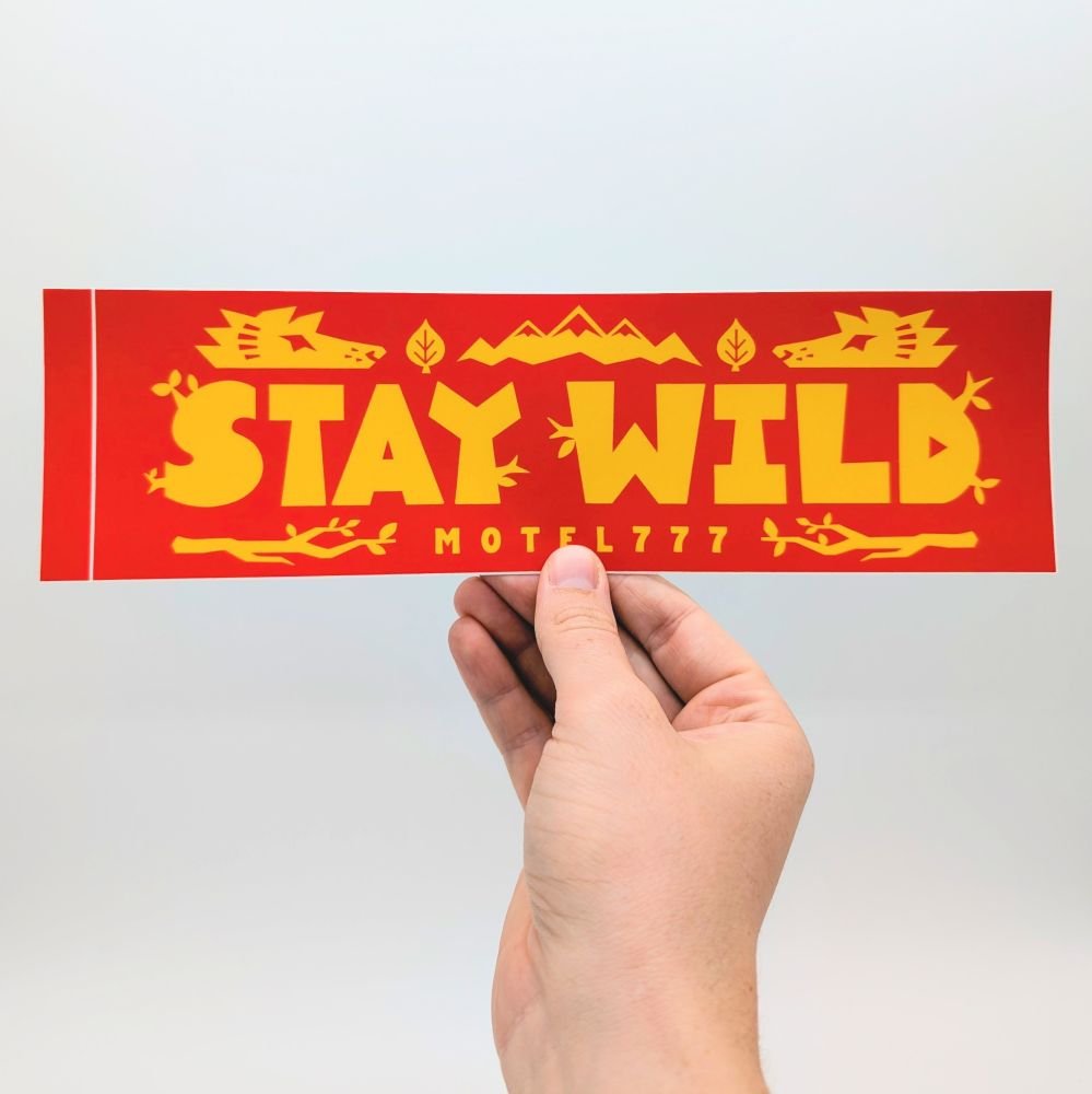 A hand holding up the Stay Wild bumper sticker.