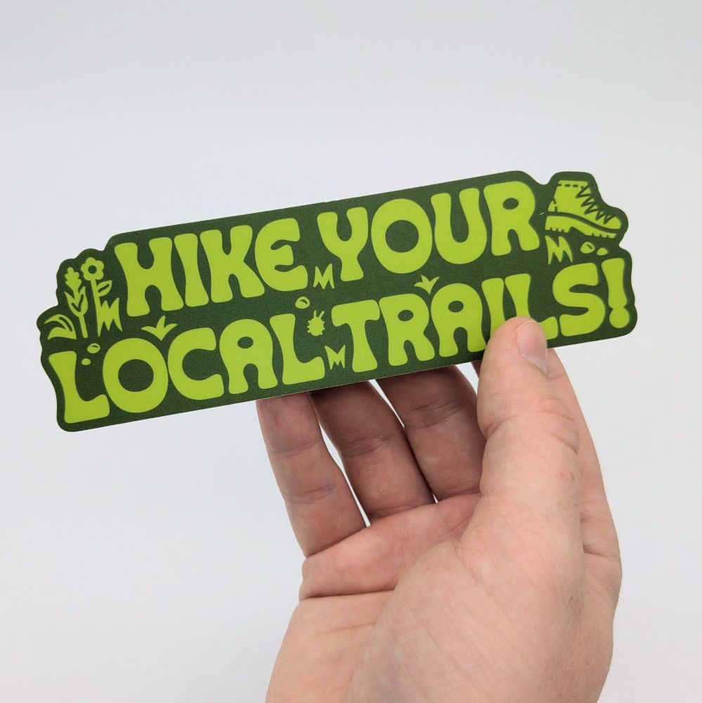 A Hike Your Local Trails sticker being held.