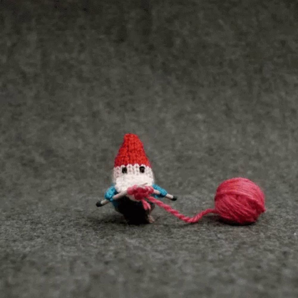 a knitted gnome is playing with a ball of red yarn