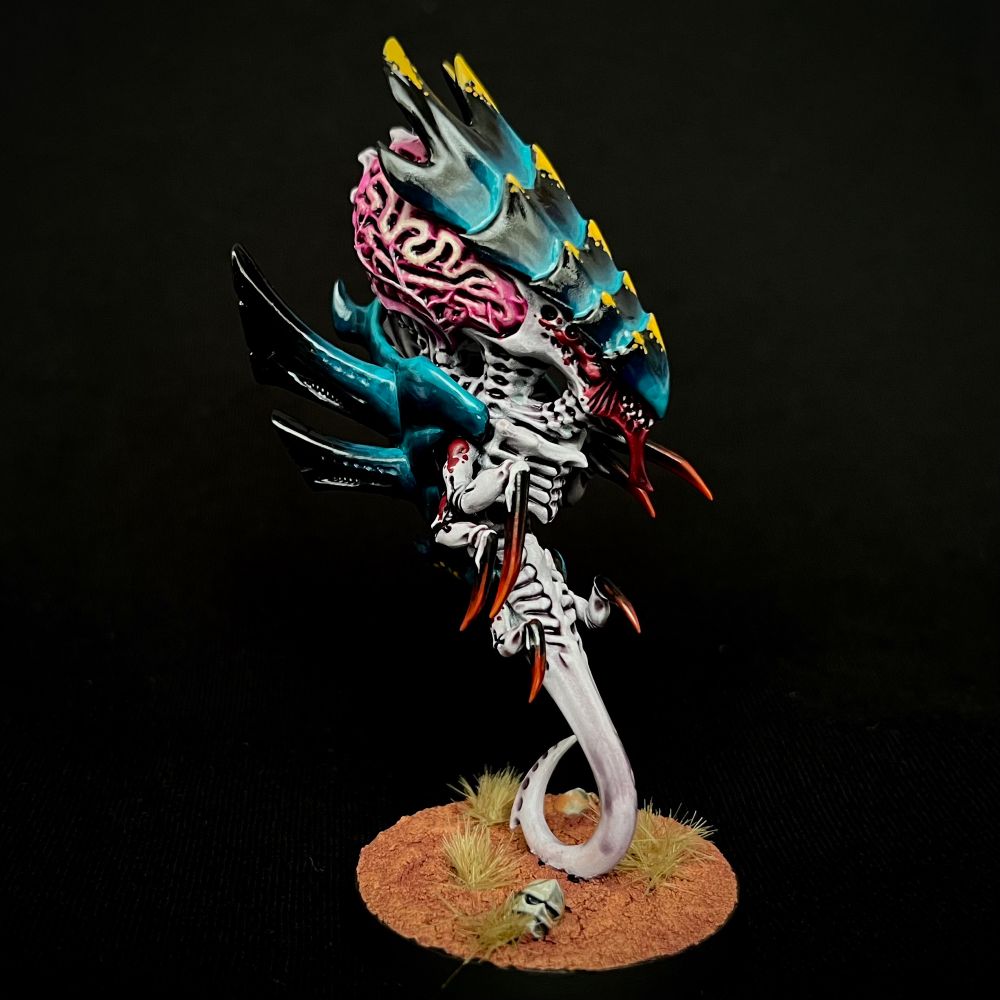 A Tyranid Zoanthrope with black and turquoise carapaces with yellow markings, whitish purple skin with red markings, and oversized glowing pink brains
