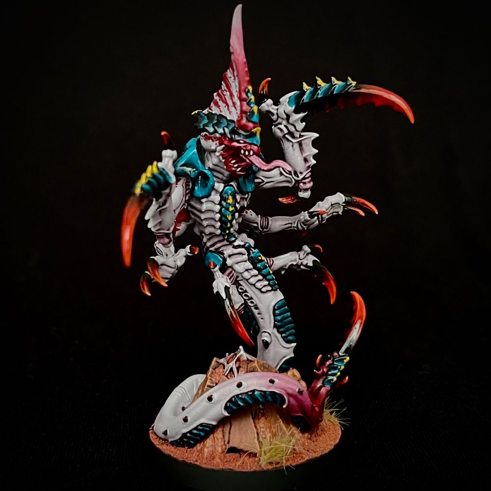 The leader of the Hyper-Adapted Raveners painted with glossy black/blue carapace with yellow markings, white/purple skin with red markings, and dark red claws and spikes. It has glowing pink/white eyes and a raised crest protruding from its head