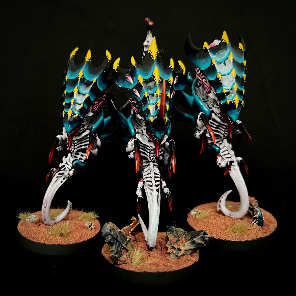 A trio of Tyranid Zoanthropes with black and turquoise carapaces with yellow markings, whitish purple skin with red markings, and oversized glowing pink brains