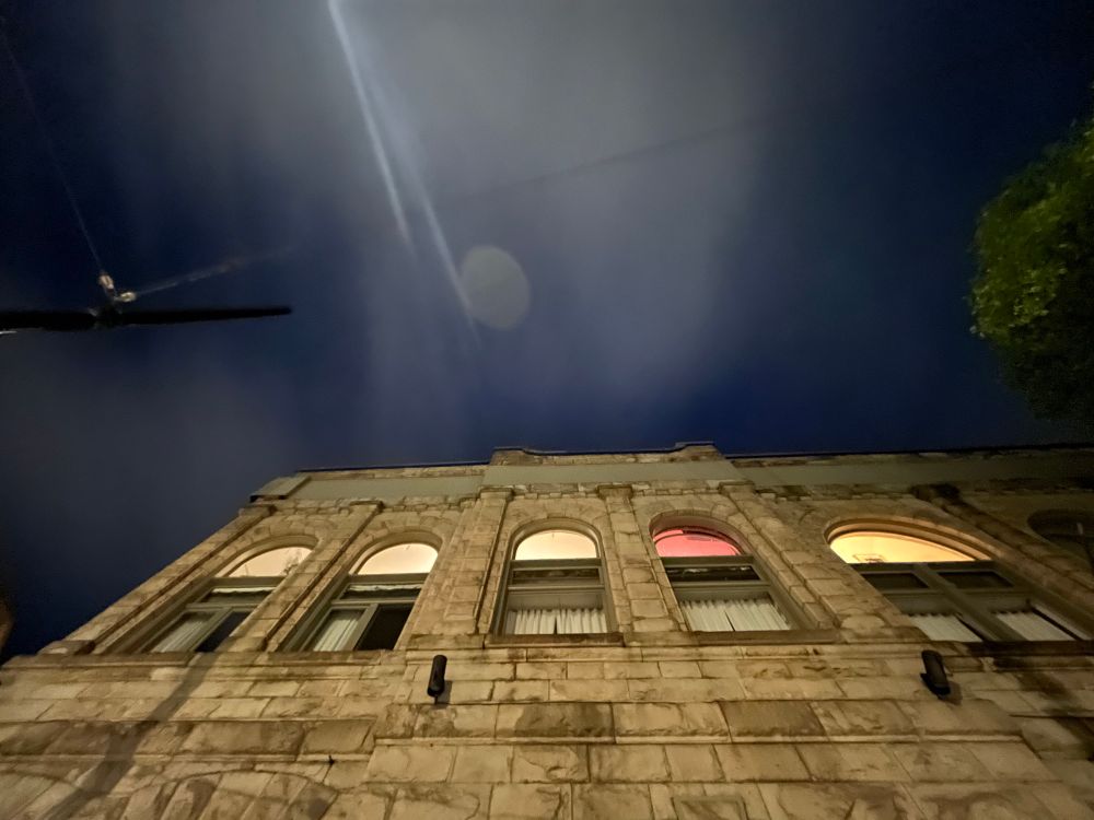 Looking up at night with a streetlight glowing against night sky and the z-Space building with all the windows still with lights on. 