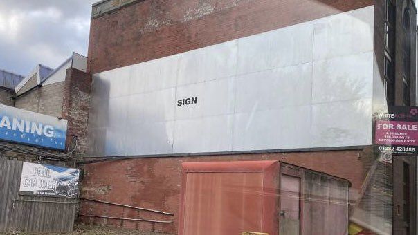 Giant blank white billboard mounted to a building with the word "SIGN" in black, centered in tiny lettering.