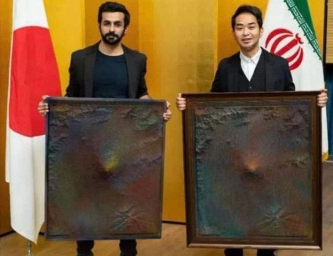 Two men standing and holding similar textured artworks in front of them, each piece with a protrusion at its center.