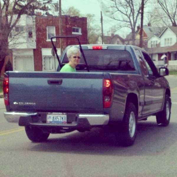 An older woman sits in the back of a pickup truck.