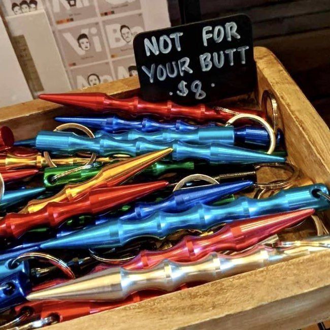A retail display box of kubaton keychain weapons with a sign that reads "NOT FOR YOUR BUTT $8."