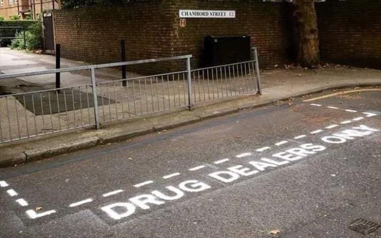 A parking space outlined with a painted white dotted line and labeled "DRUG DEALERS ONLY."