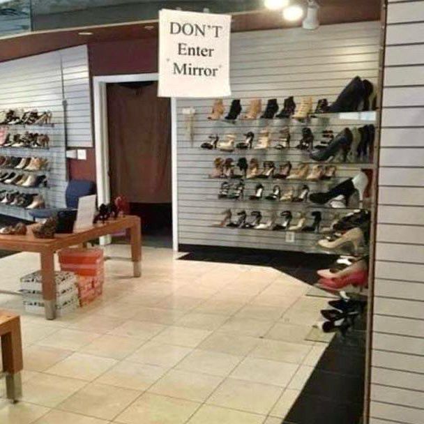 An interior view of a shoe store or department featuring a sign that reads "DON'T Enter Mirror" on a mirror covering a wall.