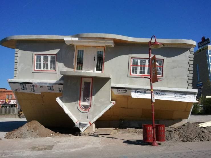 A one story house sits upside-down on a dirt lot.