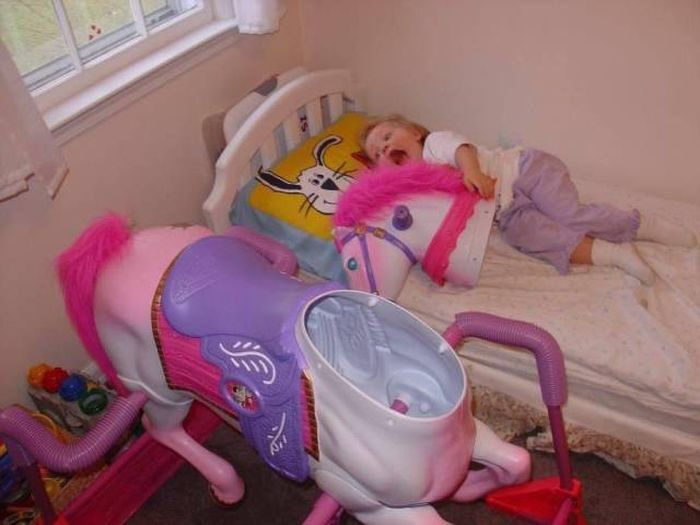 A pink and white headless rocking horse sits next to a bed. The head is in the bed next to a screaming child.