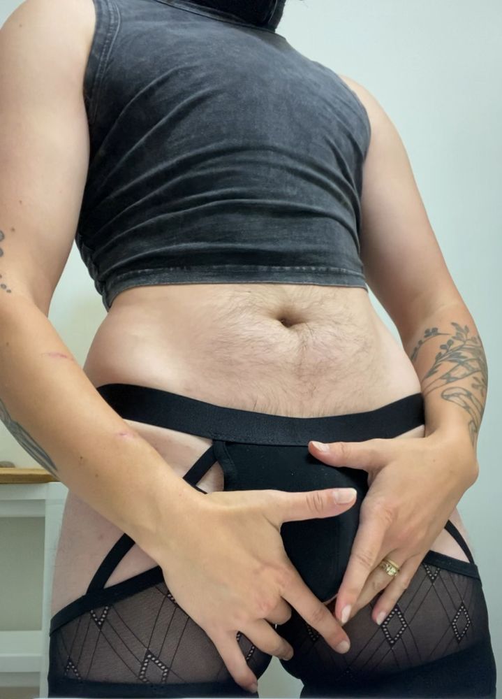 I’m standing facing the viewer center frame, the image cropped at my neck and mid thighs. I’m wearing a tight black crop top with a faded denim texture and black lace boxers with cutouts around the hips and groin, the front pocket bulging out under the stress of my cock and the soft caress of my hands.